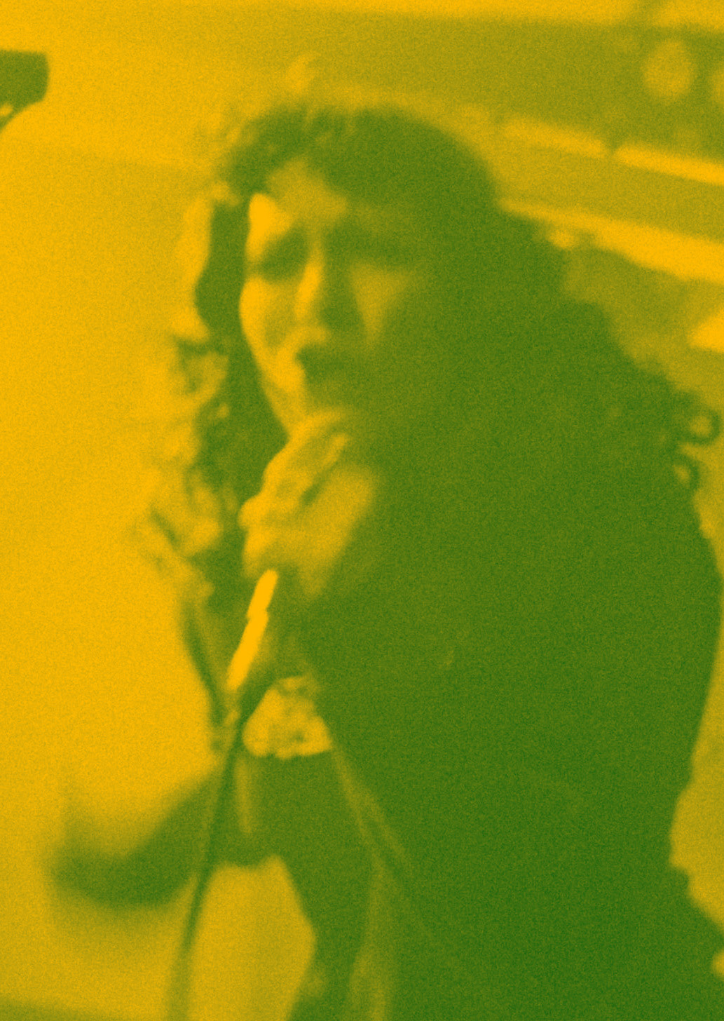 Green-yellow tinted image of Bec on stage, singing into a mic.