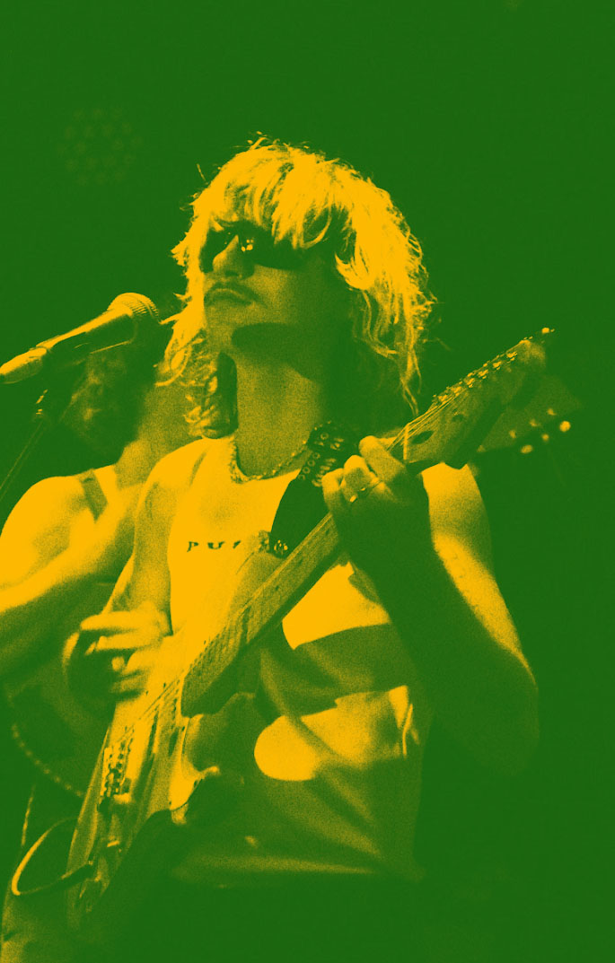 Green-yellow tinted image of Ethan on stage, strumming.