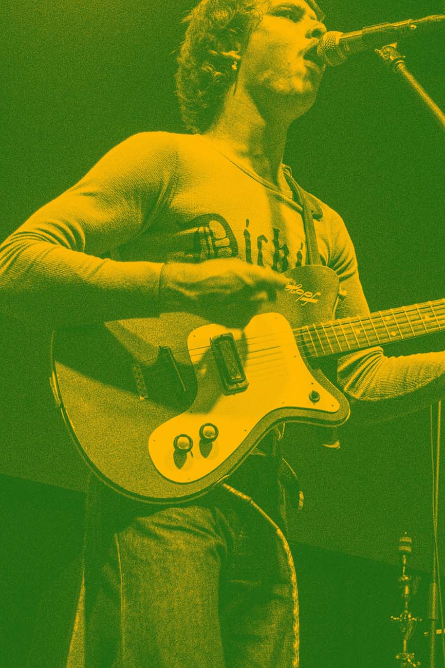 Green-yellow tinted image of Ned on stage, strumming while singing.