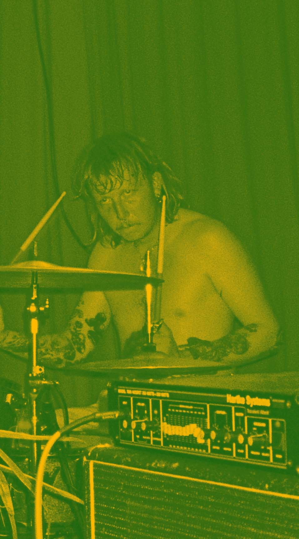Green-yellow tinted image of Van on stage, on drums.